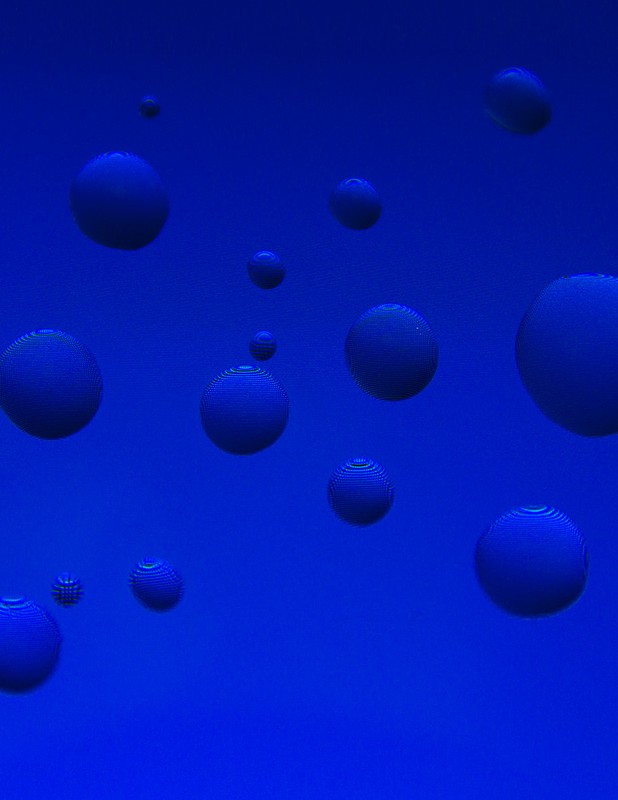 Abstract blue background featuring various sizes of dark blue spheres scattered across the frame creating a surreal, three-dimensional effect.