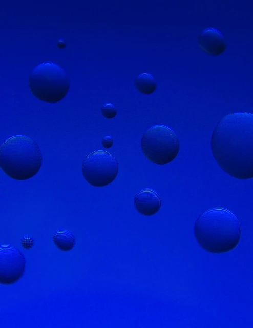 Abstract blue background featuring various sizes of dark blue spheres scattered across the frame creating a surreal, three-dimensional effect.