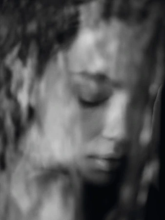Close-up monochrome portrait of a woman with closed eyes and textured hair, shot in soft focus by photographer Sesse Lind.