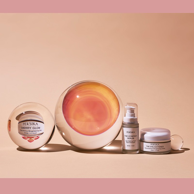 Beauty product line by Persika featuring serum, cream, and glow, displayed in transparent spheres on a light peach-colored background.