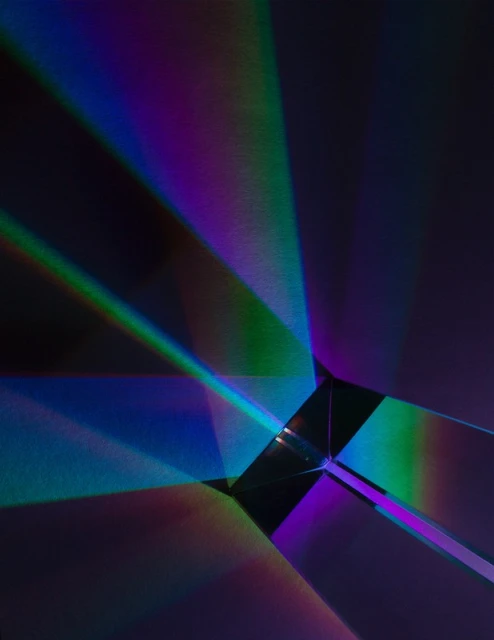 Abstract image of a prism refracting light into a spectrum of colors, creating vibrant beams against a dark, shadowed background.