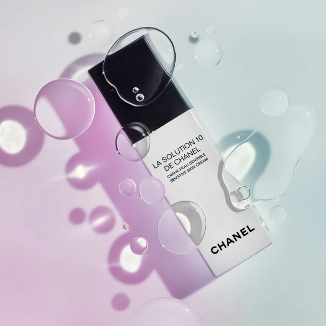 Chanel La Solution 10 de Chanel cream product shot. Bottle displayed with water droplets against a light blue to pink gradient background.