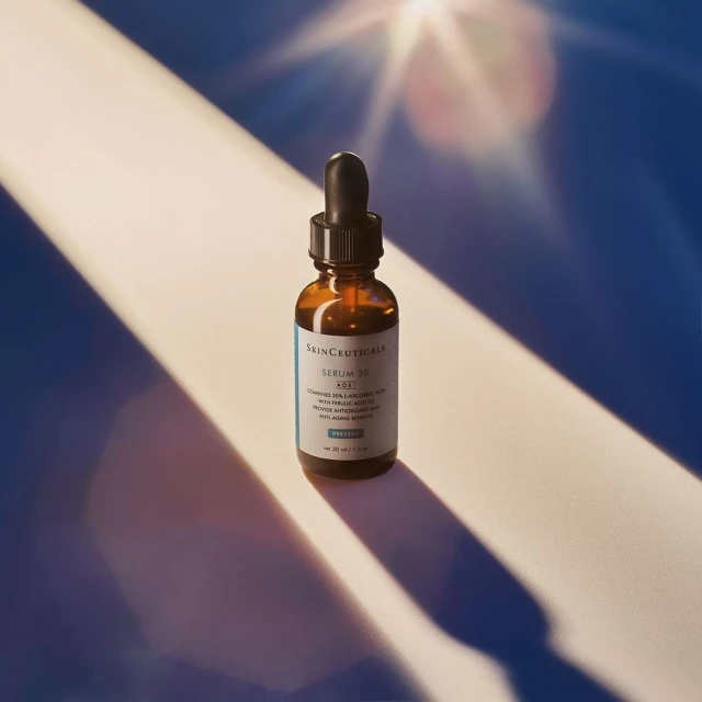 SKIN CEUTICALS Serum bottle with dropper on white surface with blue background and light flares. Beauty and skincare product photography.