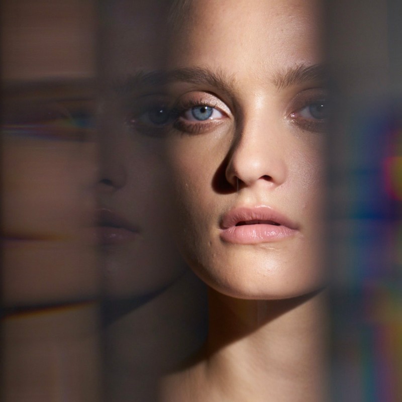 Close-up portrait of a fair-skinned woman with blue eyes looking directly forward with neutral expression, with refracted light effects.