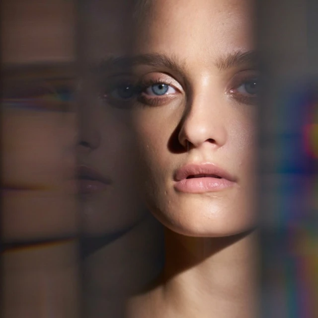 Close-up portrait of a fair-skinned woman with blue eyes looking directly forward with neutral expression, with refracted light effects.