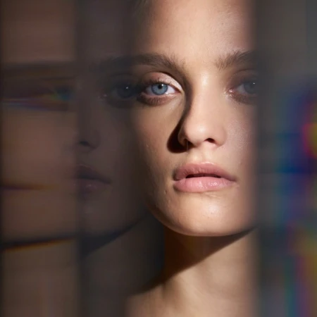 Close-up portrait of a fair-skinned woman with blue eyes looking directly forward with neutral expression, with refracted light effects.