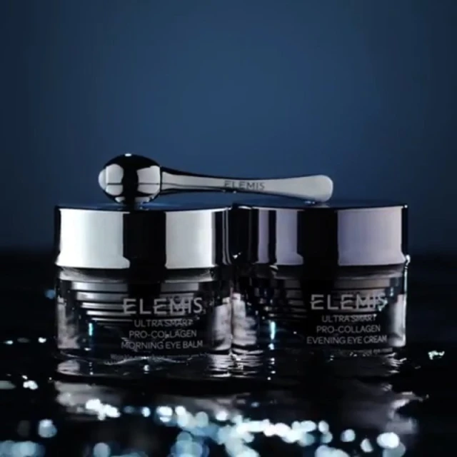 Two jars of Elemis Ultra Smart Pro-Collagen eye cream with a silver applicator against a dark blue background, beauty product.