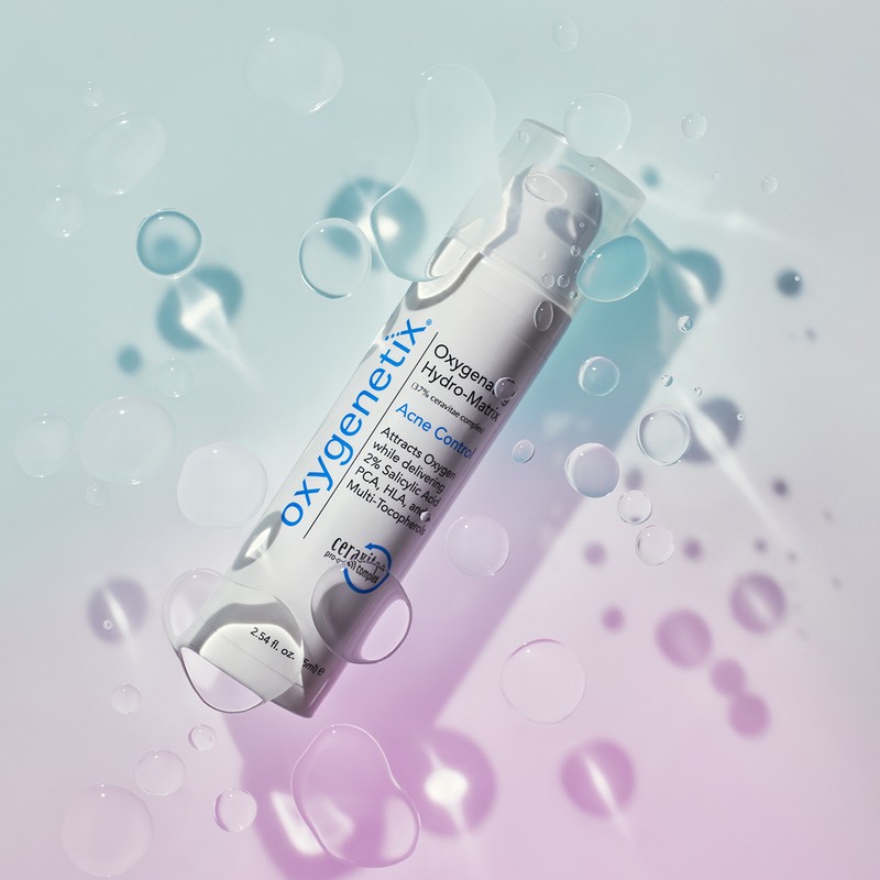 Cosmetic product, Oxygenetix Hydro-Matrix Acne Control, against a softly gradient blue and pink backdrop with water droplets.