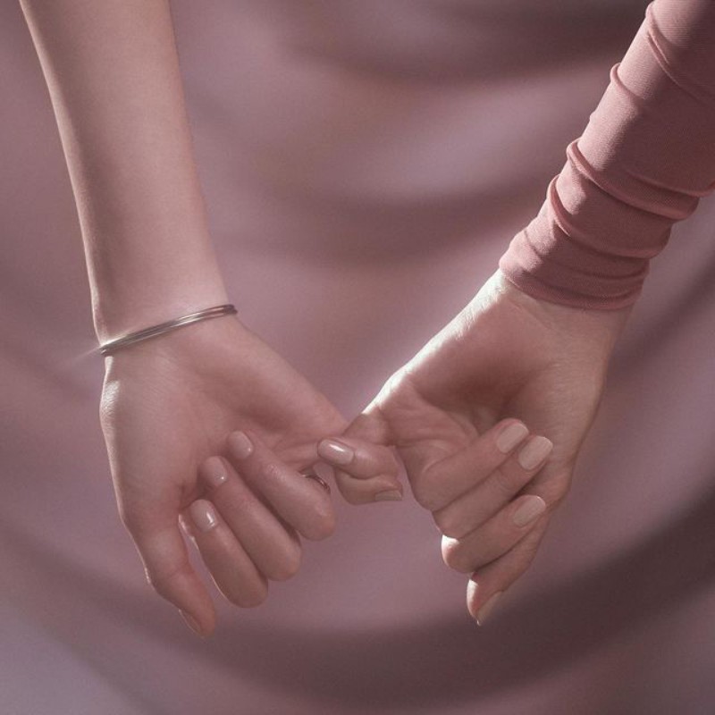 Close-up of two people holding pinky fingers together, soft lighting, and pastel colors create a gentle and intimate aesthetic.