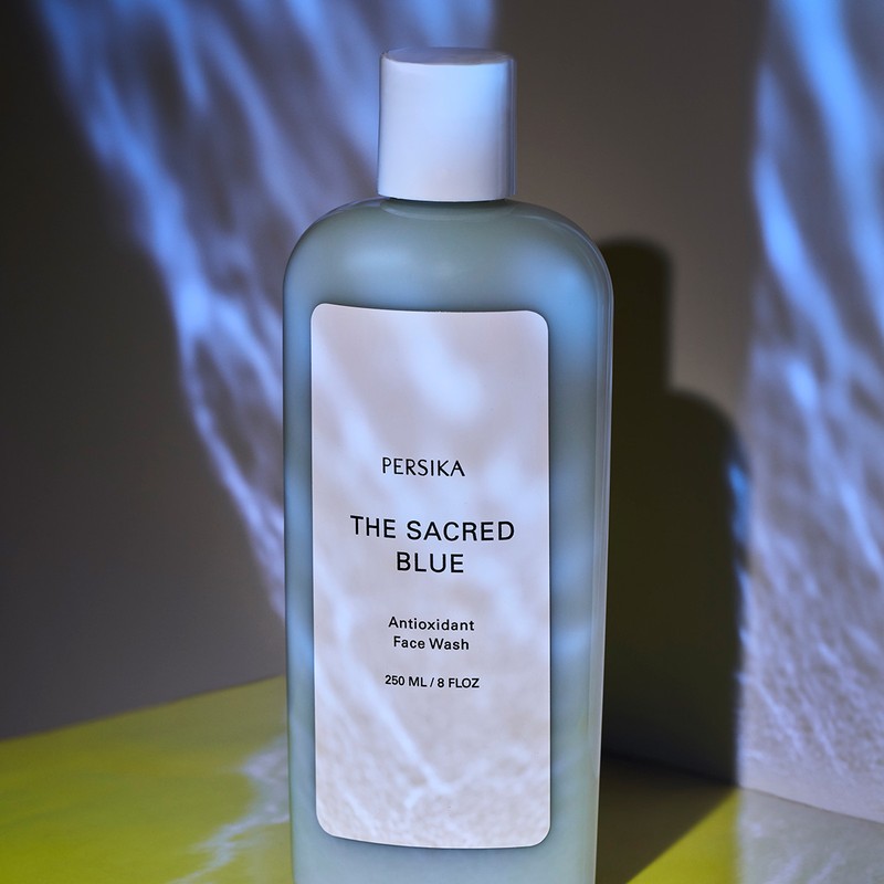Persika brand face wash in a light blue bottle with white label, set against a backdrop with blue light patterns.
