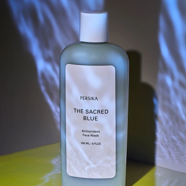 Persika brand face wash in a light blue bottle with white label, set against a backdrop with blue light patterns.