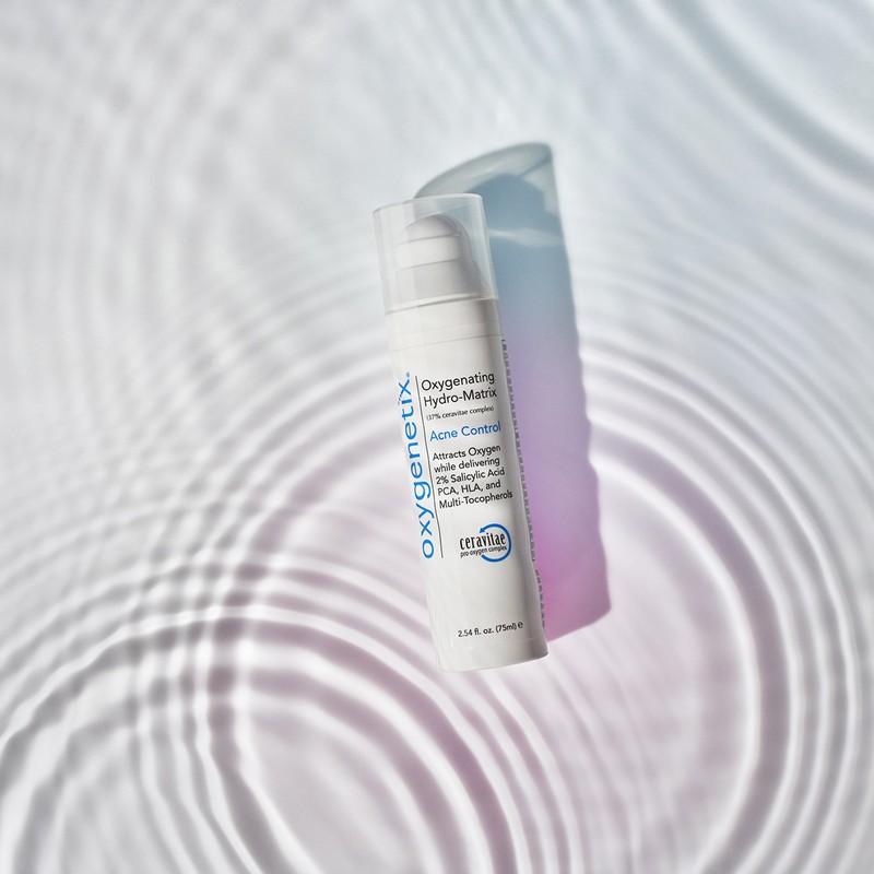 Oxygenetix Acne Control product with a soft shadow, set against a background of rippling light and shadow patterns.