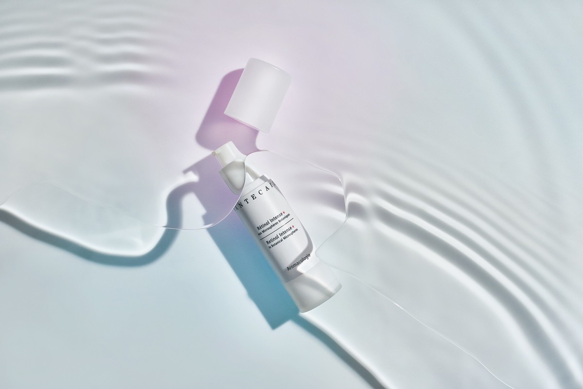 White skincare bottle with cap off on a white surface with light refracted to look like water, product shot for beauty industry.