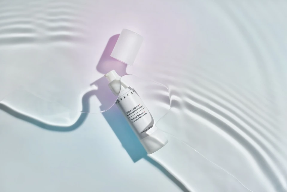 White skincare bottle with cap off on a white surface with light refracted to look like water, product shot for beauty industry.