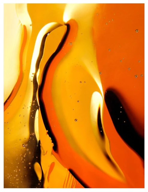 Abstract close-up photograph of fluid patterns in amber, gold, and black, with dark wavy lines flowing through a golden liquid.