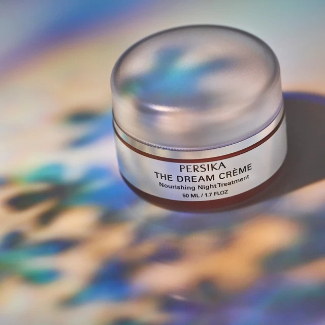 Close-up of Persika The Dream Crème container on a multicolored surface with lighting effects, ideal for beauty advertising.