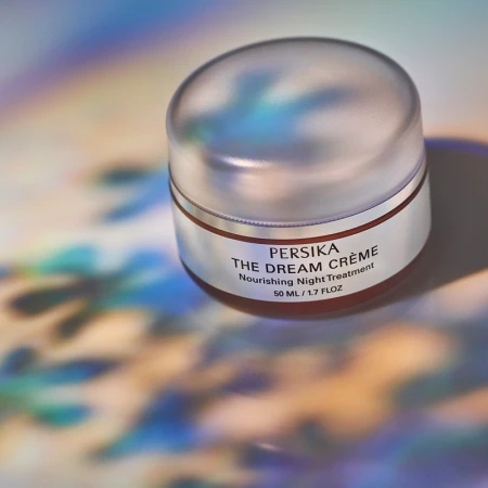 Close-up of Persika The Dream Crème container on a multicolored surface with lighting effects, ideal for beauty advertising.