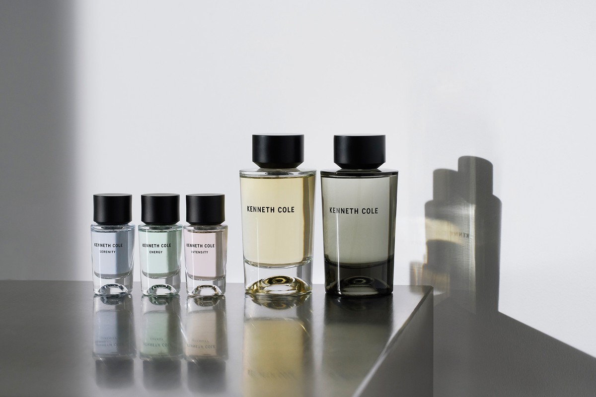 A row of Kenneth Cole fragrance bottles in varying sizes and colors on a reflective gray surface, set against a plain white background.