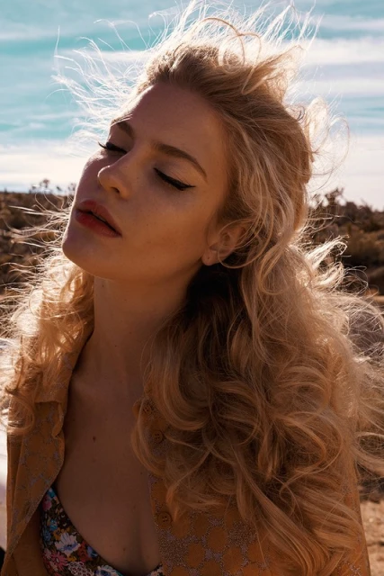 Portrait of a blonde woman with closed eyes standing outdoors. Wind is blowing through her hair in a sunny desert environment.