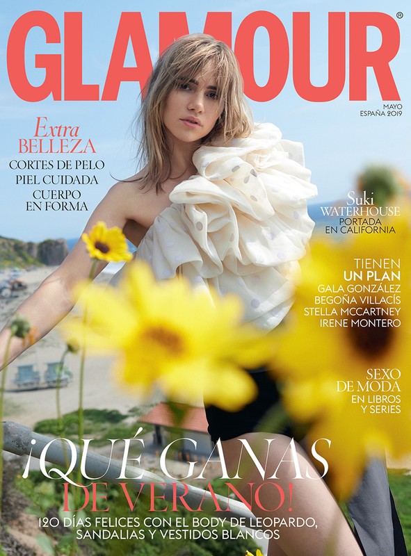 Glamour magazine cover featuring Suki Waterhouse in a ruffled top amidst sunflowers and a coastal backdrop on a sunny day.