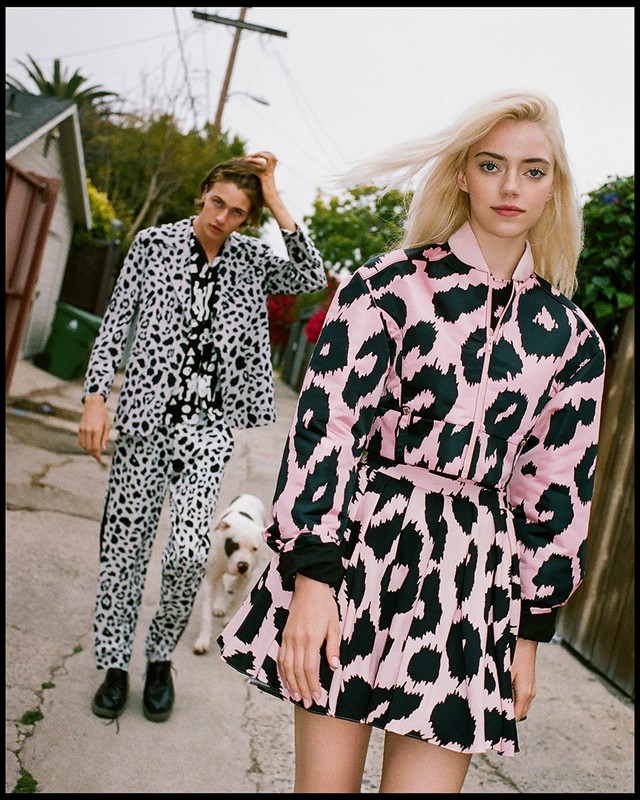 Two fashion models, one male and one female, wearing matching black and white and pink and black animal print outfits, outside.