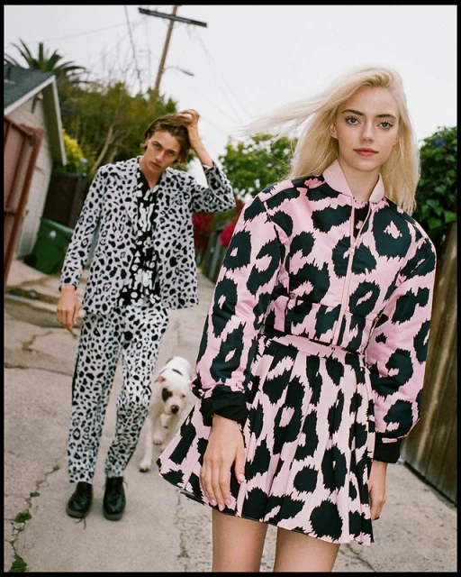 Two fashion models, one male and one female, wearing matching black and white and pink and black animal print outfits, outside.