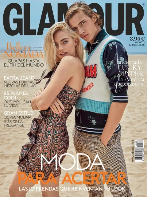 Glamour magazine cover features a blonde woman in a patterned dress and a blonde man in a sweater vest on a beach backdrop.