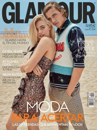 Glamour magazine cover features a blonde woman in a patterned dress and a blonde man in a sweater vest on a beach backdrop.