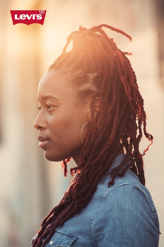 A profile shot of an African-American woman with locs, wearing a denim shirt in outdoor lighting, with the Levi's logo visible.