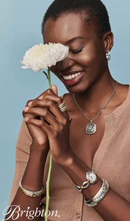 Black woman with short hair holding a white flower in front of her face, wearing jewellery and a brown ribbed top.