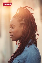 Black woman in profile with long dreadlocks wearing a denim shirt in warm sunlight with Levi's logo