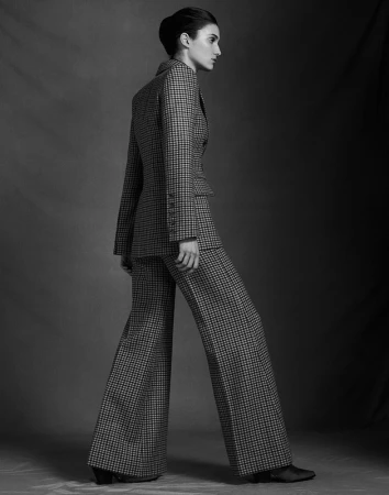 Monochrome portrait of a model standing in profile wearing a houndstooth blazer and flared trousers with hair styled in an updo.