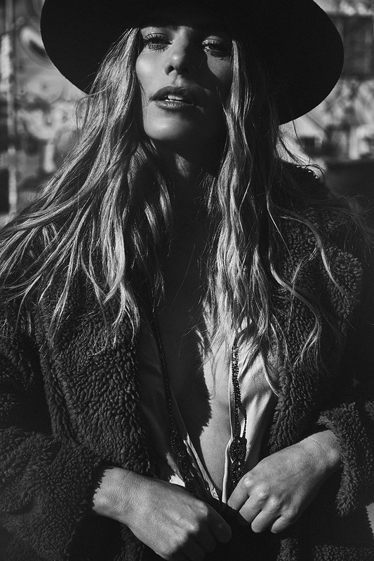 Monochrome portrait of a blonde woman in a hat and open jacket. The woman is facing forward, with the sun shining on her face.