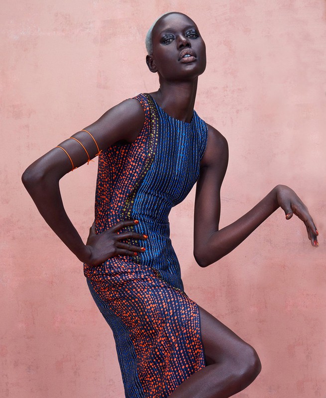 Fashion shot of a Black female model posing in a printed sleeveless dress against a pink background in a studio setting.