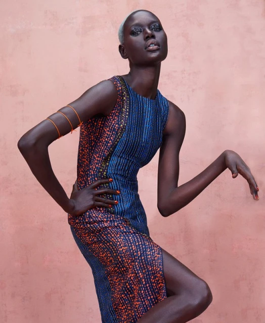Fashion shot of a Black female model posing in a printed sleeveless dress against a pink background in a studio setting.