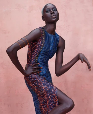 Fashion shot of a Black female model posing in a printed sleeveless dress against a pink background in a studio setting.