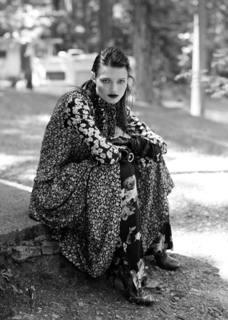 Black and white portrait of a woman in a floral dress and dark lipstick seated outdoors on a stone step