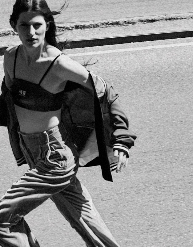 Woman in bra top and bomber jacket running on city street in a black and white fashion shot with a shallow depth of field.