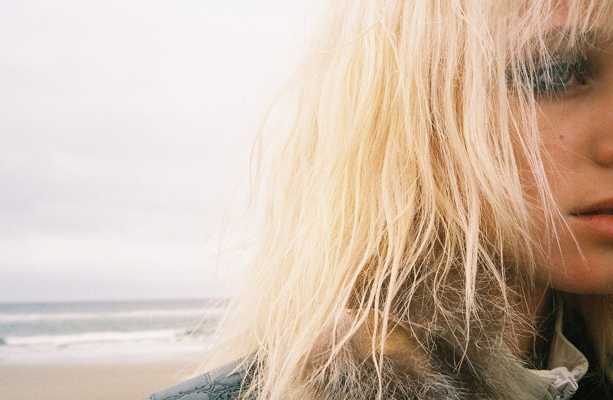 Close-up portrait of a blonde woman with textured hair by the ocean, featuring styling by Sirsa in Los Angeles.
