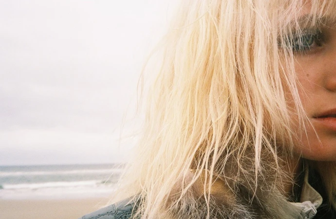 Close-up portrait of a blonde woman with textured hair by the ocean, featuring styling by Sirsa in Los Angeles.