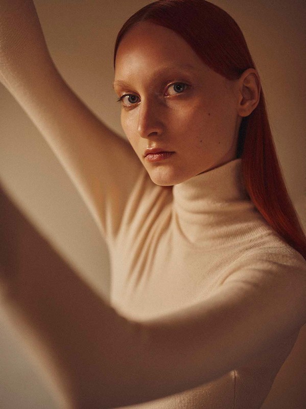 Portrait of a red-haired woman wearing a turtleneck, posing in a studio with soft lighting and a neutral background. Fashion and beauty shot.