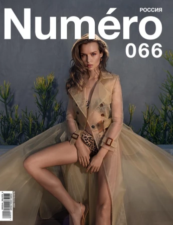 Model seated outdoors in a sheer tan trench coat over leopard print underwear against a textured grey wall