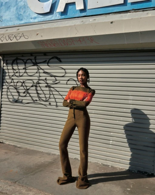 Woman poses in front of a graffitied storefront, wearing a rust-colored top, olive long sleeves, and matching high-waisted pants.