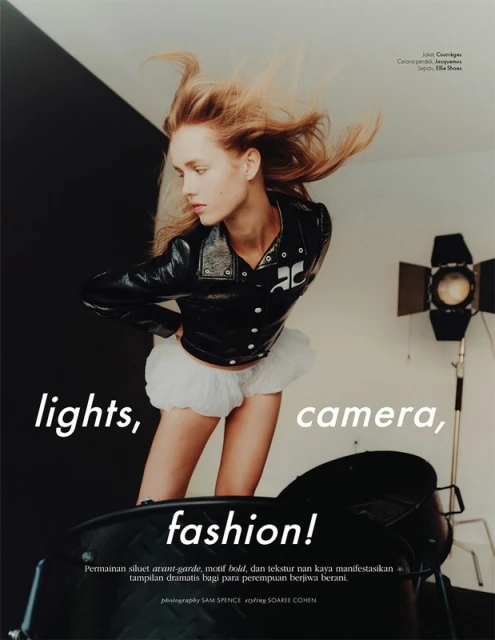 Fashion shot featuring a woman in a black jacket and white skirt, lights, camera, and fashion text overlayed on the image, studio lighting.