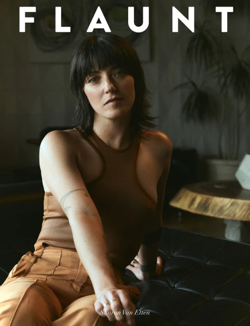 Portrait of adult female with dark hair wearing a brown top and tan pants, sitting indoors with muted, natural lighting. Magazine cover.