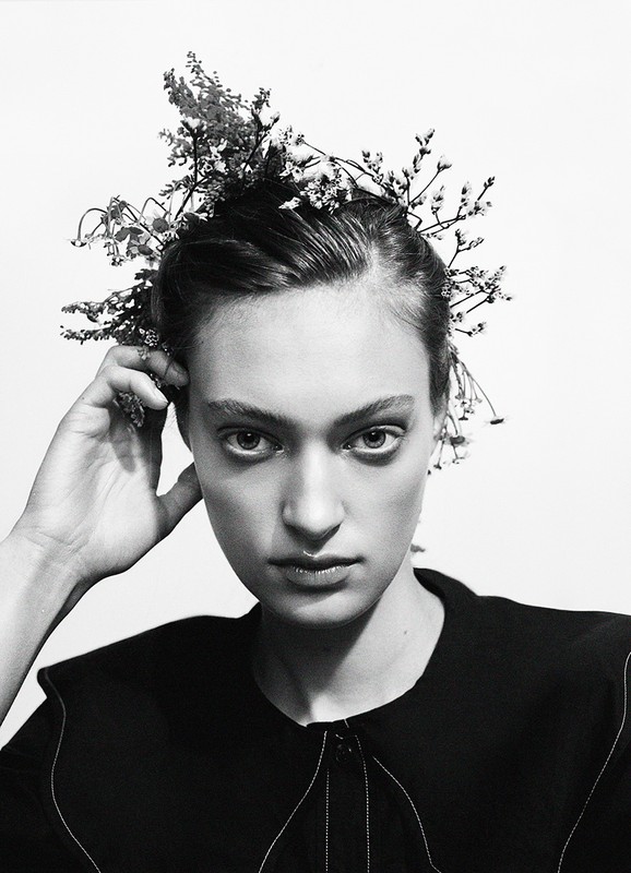 Monochrome close-up of a woman with floral headpiece, gazing directly at the camera against a stark white background, studio lighting.