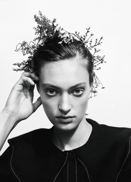 Monochrome close-up of a woman with floral headpiece, gazing directly at the camera against a stark white background, studio lighting.