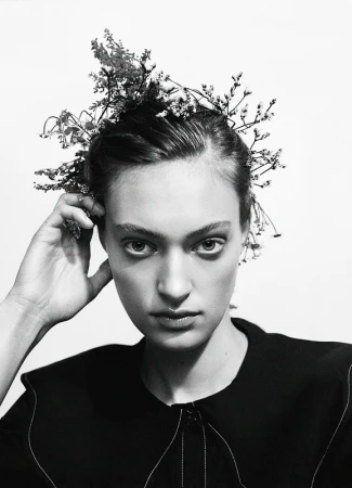 Monochrome close-up of a woman with floral headpiece, gazing directly at the camera against a stark white background, studio lighting.