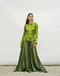 Model wearing a vibrant green textured long-sleeve shirt and matching green satin wide-leg trousers posing in front of a white backdrop.