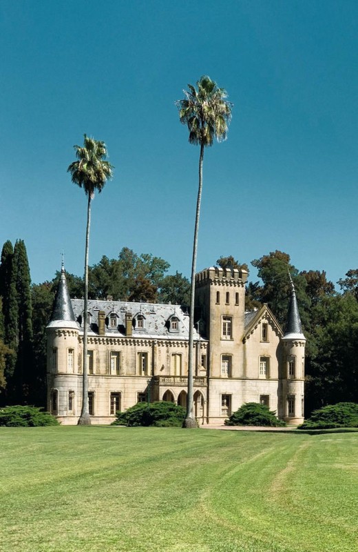Exterior view of a large, multi-level chateau-style building with towers and palm trees in a sunny, outdoor, daytime environment.